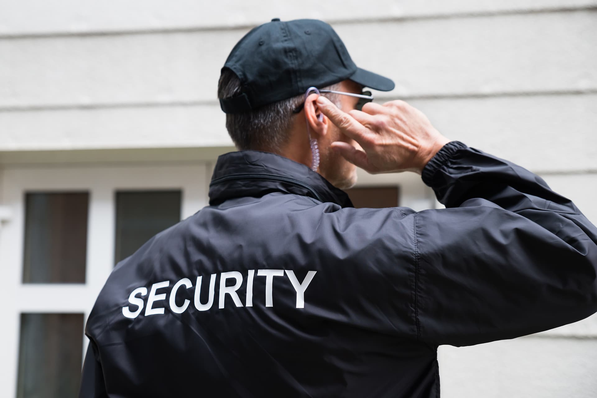 a manned security guard stationed outside a house speaking into an earpiece